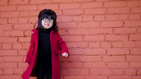 korean girl in a red coat and cap and round glasses dance on red brick wall the street in autumn