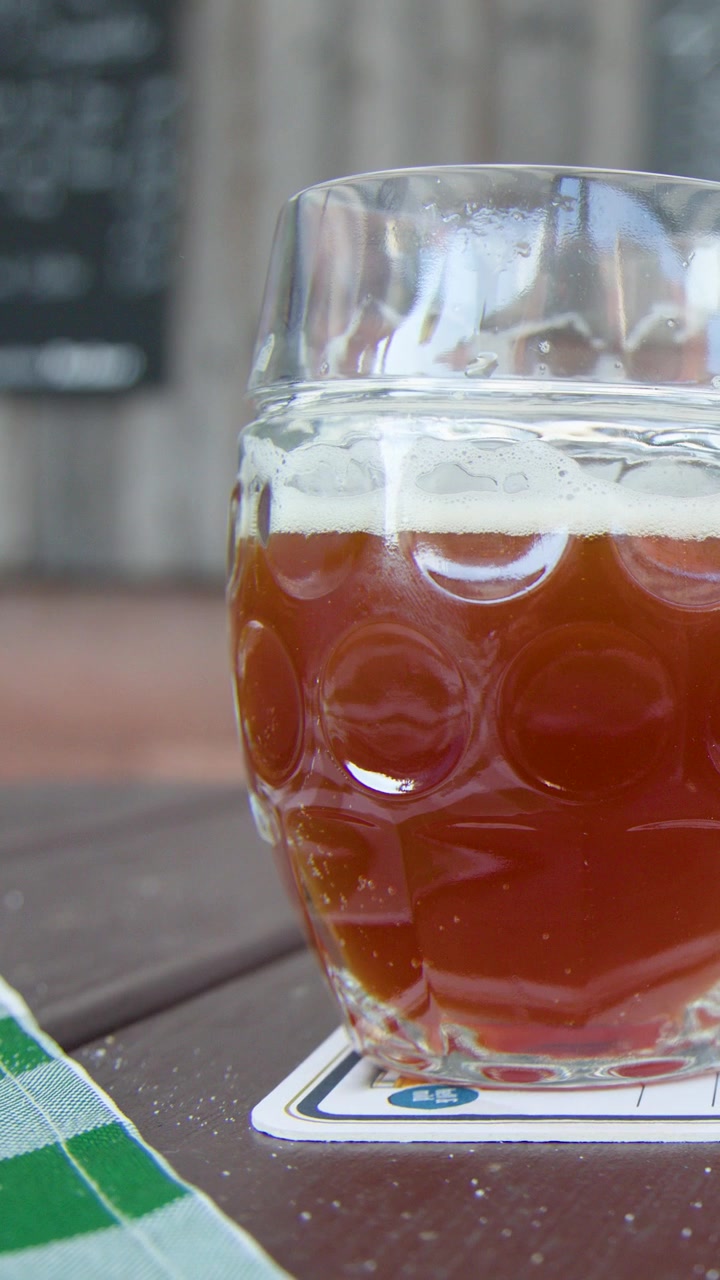 Mano che si allunga per prendere un boccale di birra tradizionale su un tavolo di legno all'aperto alla luce del giorno