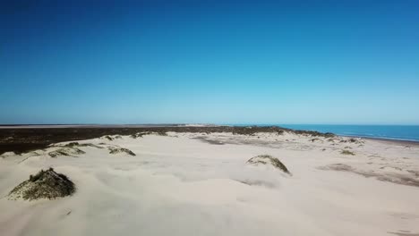 Aerial-drone-high-view-of-sand-dunes-on-gulf-shore-barrier-island-on-a-sunny-afternoon,-the-Gulf-of-Mexico-is-visible-in-the-distance---South-Padre-Island,-Texas