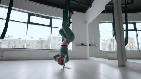 young smiling woman practice in aero stretching swing. aerial flying yoga exercises practice in green hammock in fitness club