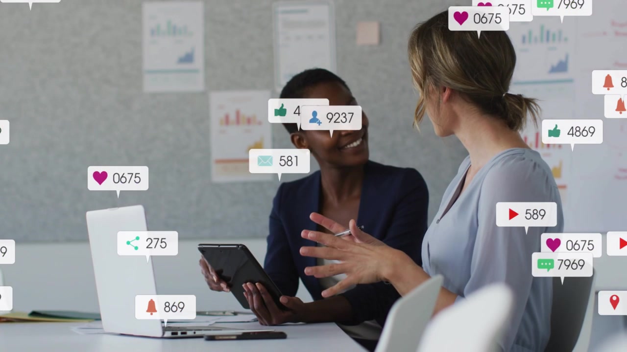Two women speaking causing social icons popping grouping thinning around tablet for marketing
