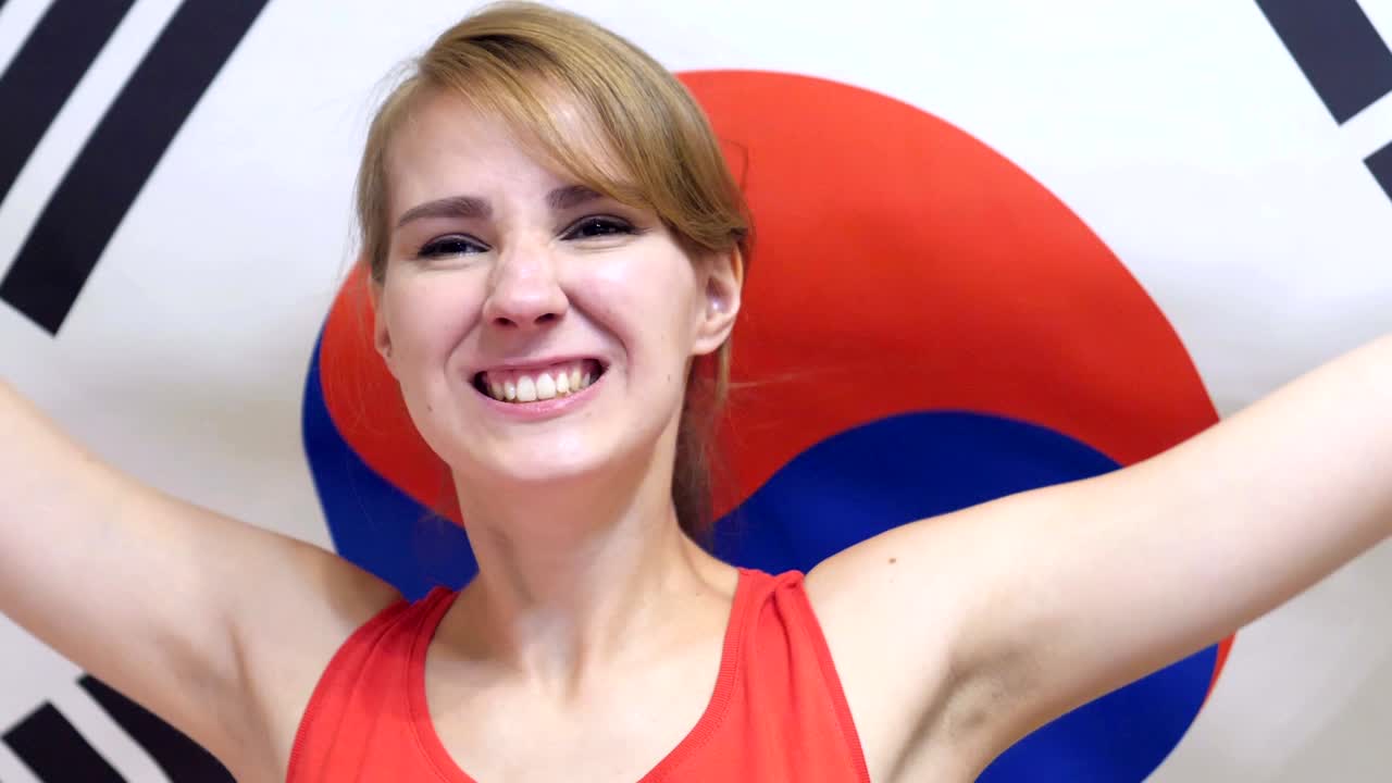 한국의 젊은 여성이 느린 동작으로 한국의 발을 들고 축하하고 있습니다.