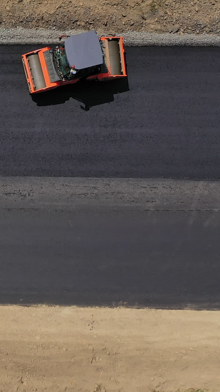 Road roller machine rolls asphalt. Aerial view on the road rollers working on the new road construction site Vertical video