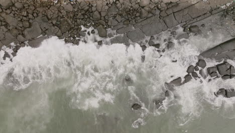 imágenes aéreas de arriba hacia abajo de las olas del océano chocando contra las rocas