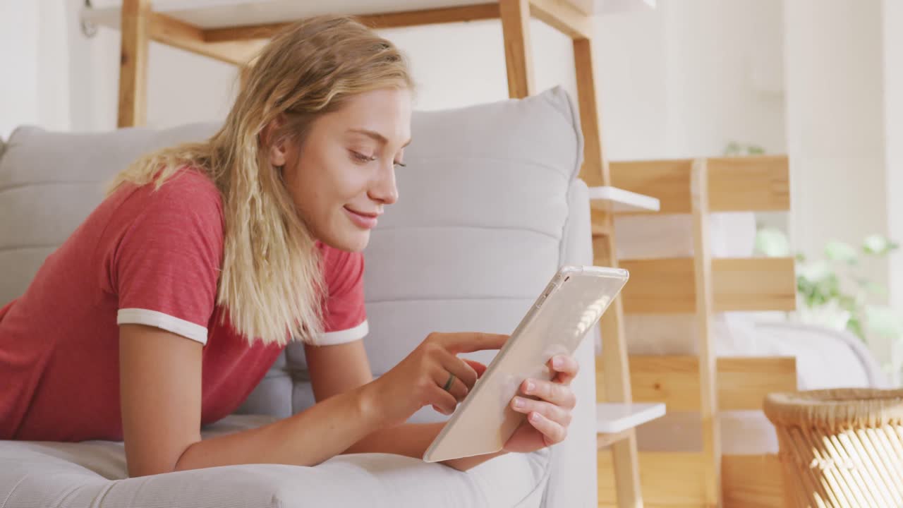 Beautiful woman using digital tablet while laying on the couch