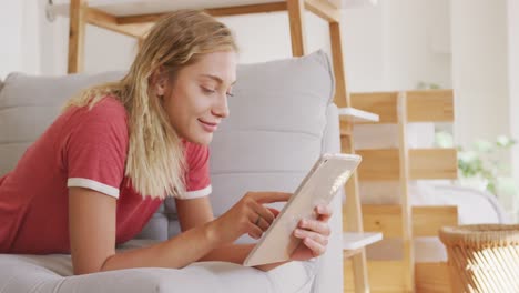 hermosa mujer usando una tableta digital mientras está acostada en el sofá