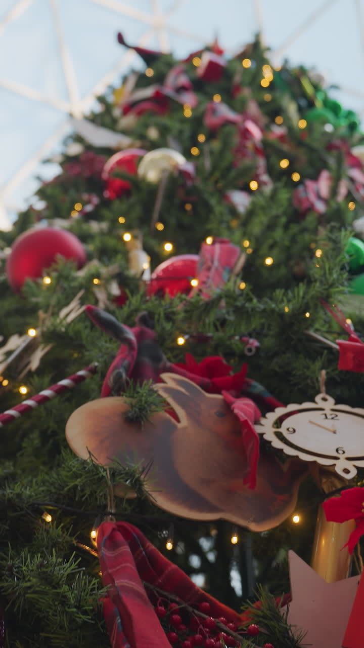 Close-up of beautifully decorated Christmas tree with glowing lights, red and gold ornaments, Santa figurine, gift boxes, and festive decorations creating a warm holiday atmosphere