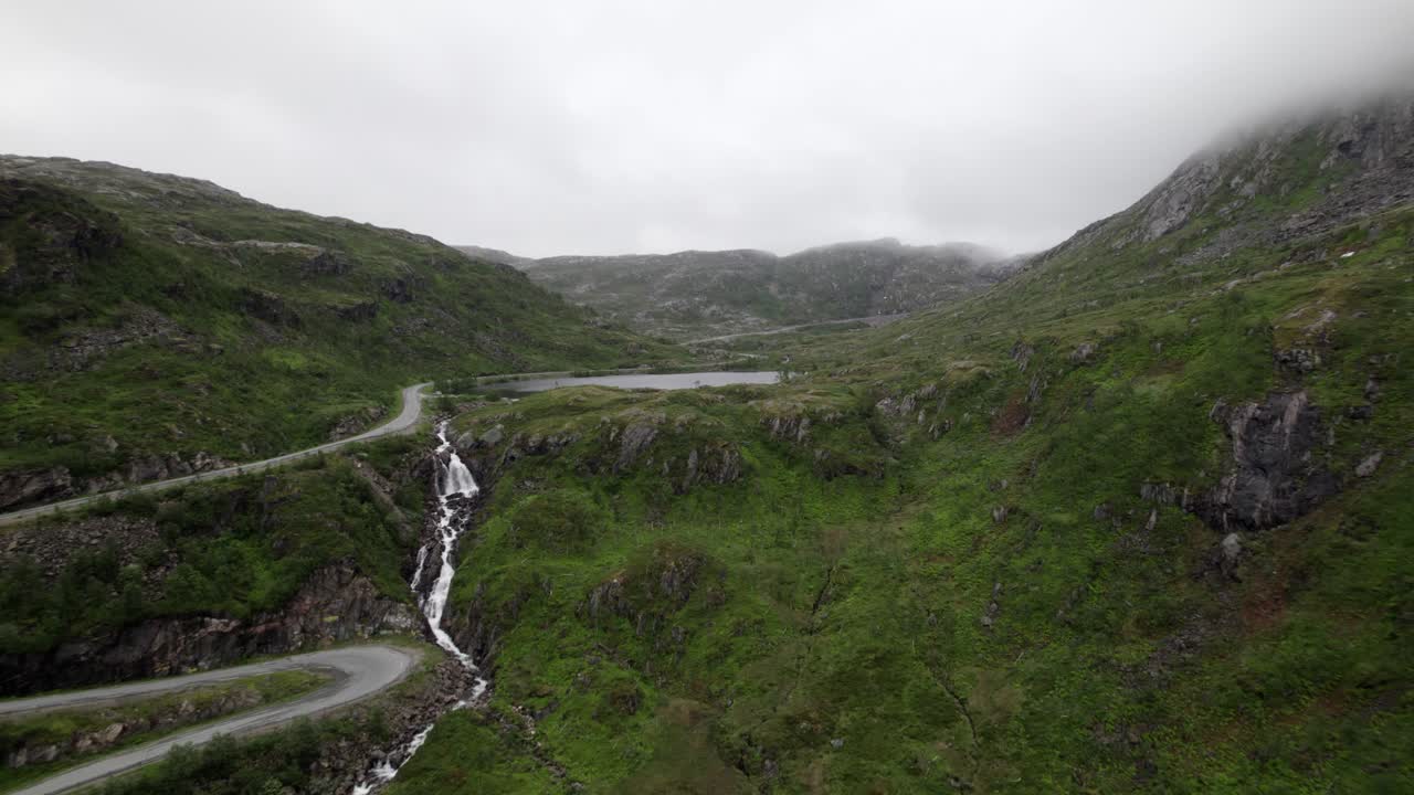 volando hacia la cascada y el lago al lado de una pequeña carretera en un estrecho valle en senja en noruega