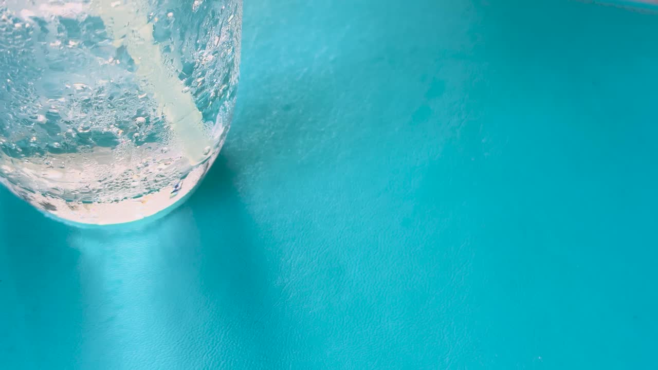 primer plano de refresco de club con limón y hielo, mostrando burbujas que se elevan en un vaso contra un fondo azul vibrante