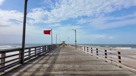wooden pier stretching into the ocean under a cloudy sky with a red flag