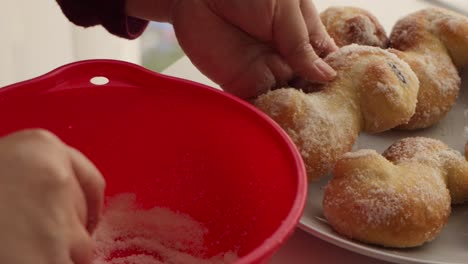 hands putting sugar from a red bowl on delicious fresh christmas buns