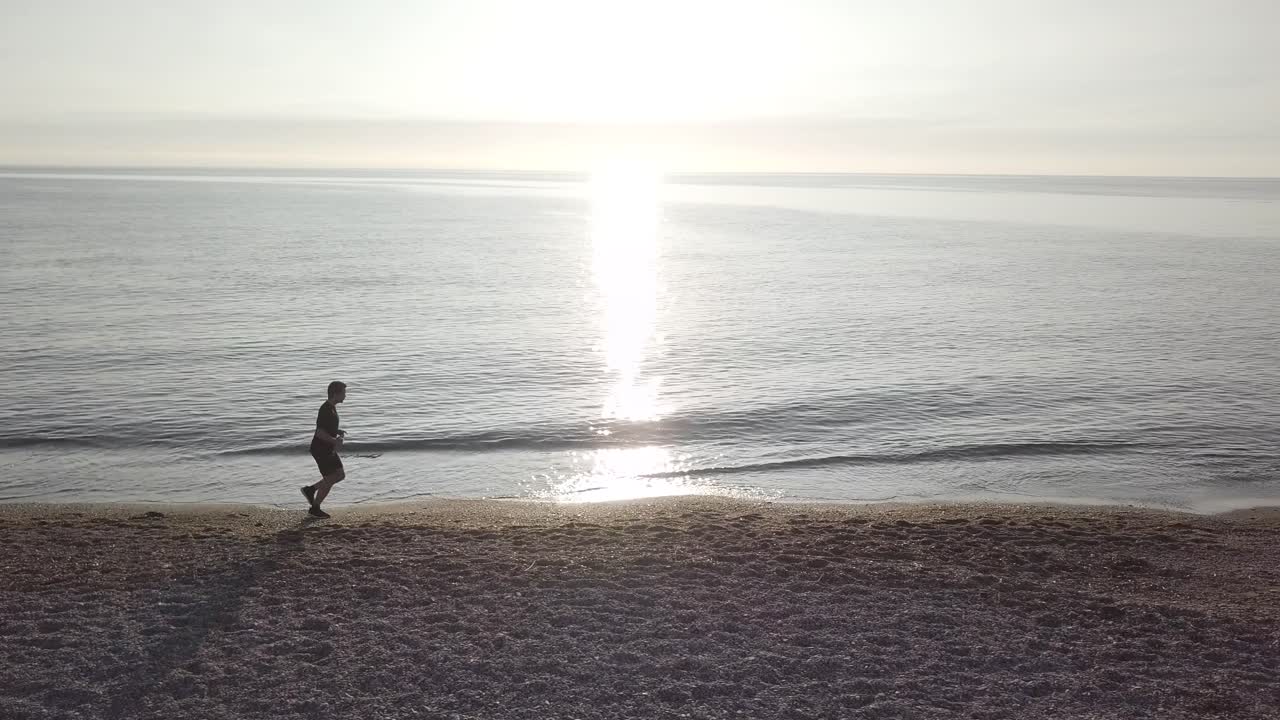 Young runner man training on beautiful sunset at beach. Drone tracking