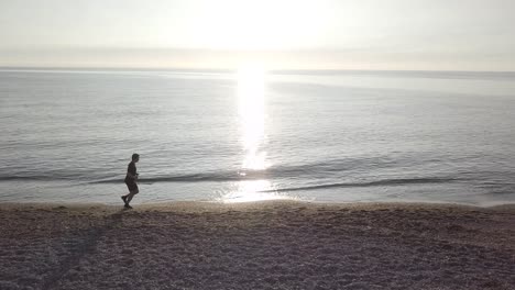 young runner man training on beautiful sunset at beach. drone tracking