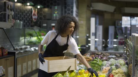 multiracial worker in black apron stocking yellow peppers in supermarket