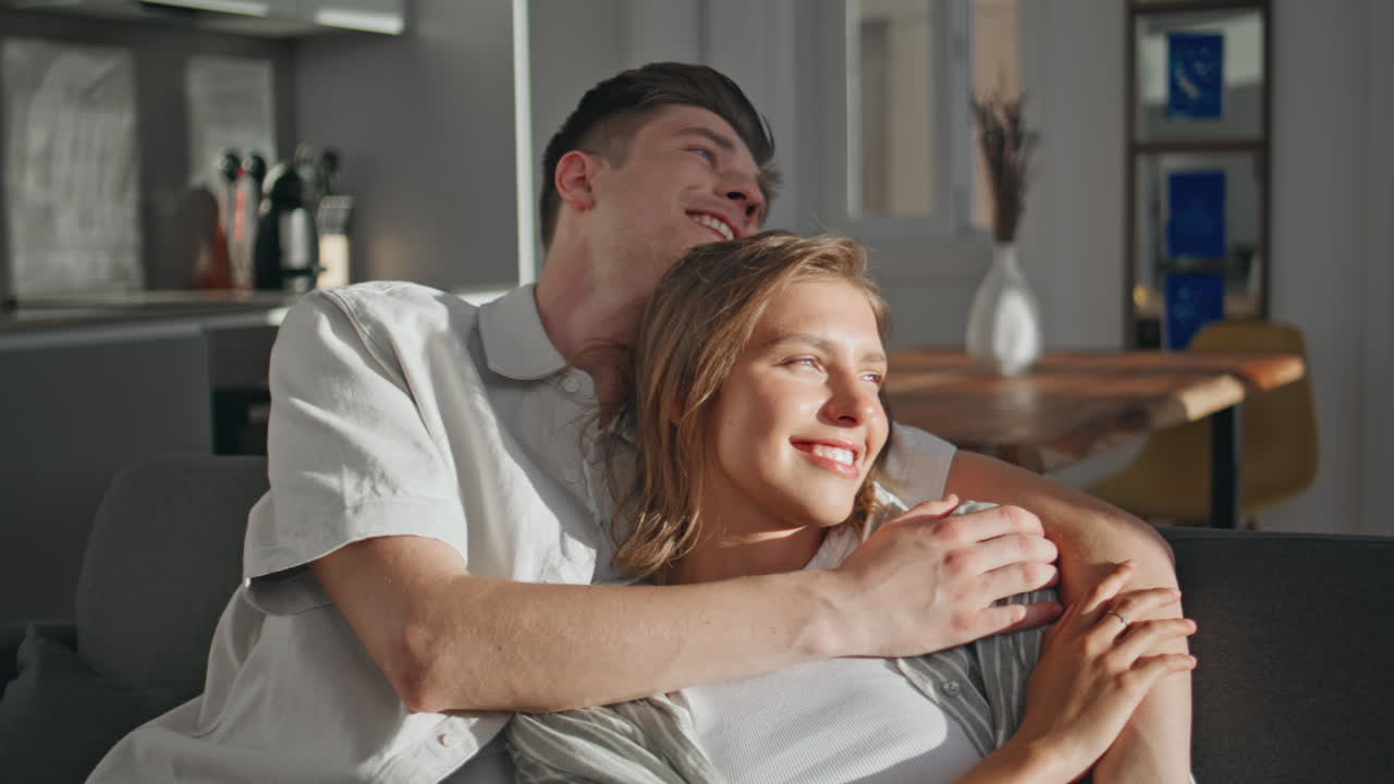 Spouses cuddling modern apartment in sunlight. Closeup relaxed people talking