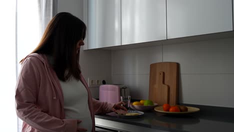 pregnant woman snacking a healthy small corn tortilla with ham and drinking some water in the kitchen