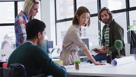 diverse office colleagues wearing face masks discussing over blueprint plan at modern office