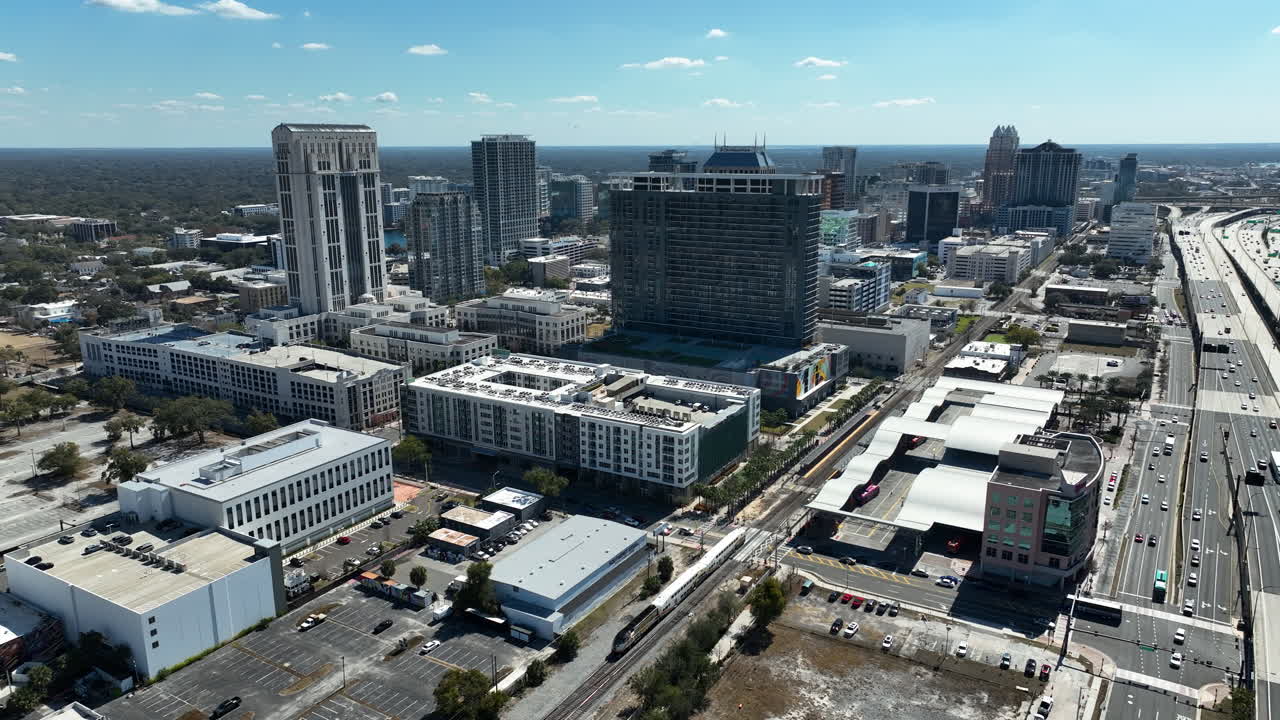 Clip drone con effetto parallasse che orbita sullo skyline del centro di Orlando mentre un treno attraversa in un pomeriggio trafficato.