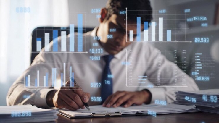 Profesjonell forretningsmann analyserer finansielle rapporter og tar notater på kontoret, omgitt av grafer og datavisualiseringer på et moderne skrivebord