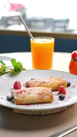 ukrainian nalysnyky revealing golden crepes topped with ripe raspberries, blueberries, dusted powdered sugar, complemented by citrus juice on pristine plate