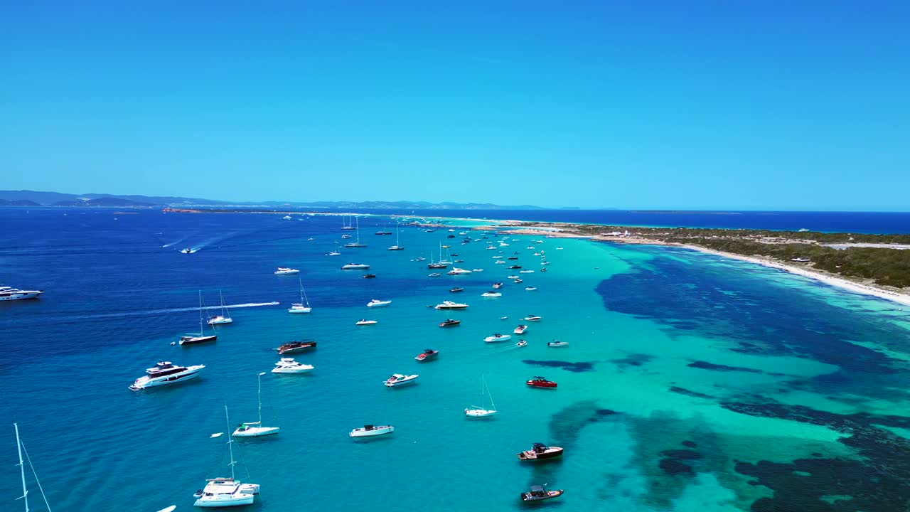 Barche ormeggiate nelle splendide acque turchesi e cristalline di Formentera, una spiaggia di sabbia bianca con Posidonia oceanica. Spettacolare vista aerea con panoramica discendente ripresa da drone