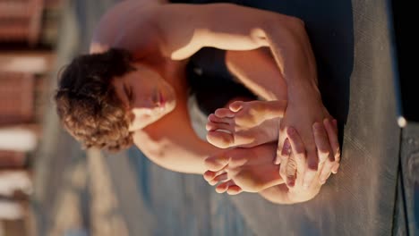 A-young-brunette-guy-in-black-shorts-is-stretching-on-a-sunny-beach.-Close-up-shot-of-a-young-guy-doing-morning-exercises