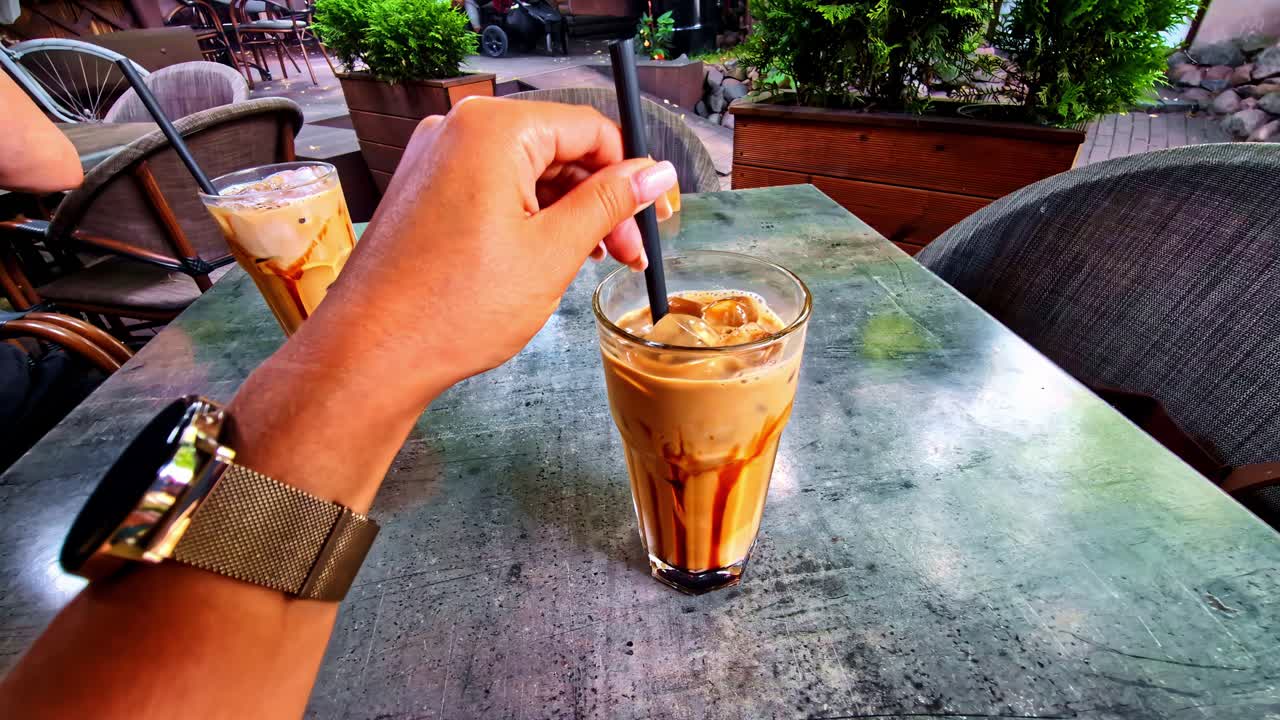 Close up of a hand wearing watch, stirring a refreshing cold coffee in a cafe setup