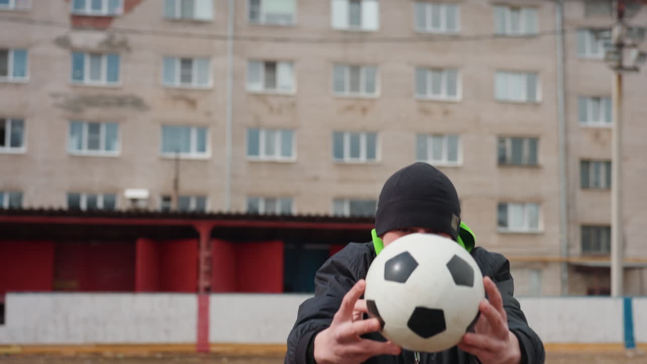 Jugador con balón y fondo urbano, atleta mostrando el balón en un entorno urbano con gran concentración, futbolista mostrando el balón frente a un entorno urbano con elementos característicos de la calle