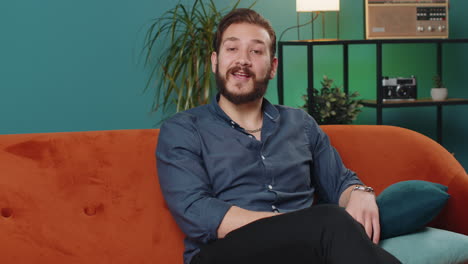 lebanese man smiling friendly at camera, waving hands gesturing hello, hi, greeting at home on sofa