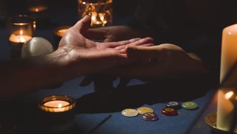 Cerca-De-Una-Mujer-Leyendo-La-Palma-De-La-Mano-Del-Hombre-Sobre-Una-Mesa-A-La-Luz-De-Las-Velas