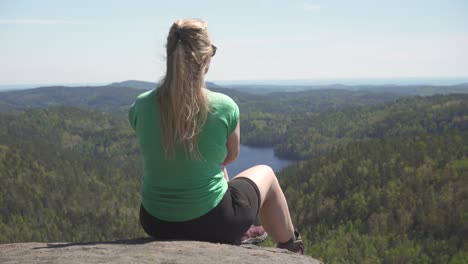 lone woman is resting on mountain viewpoint during windy summertime in southern norway