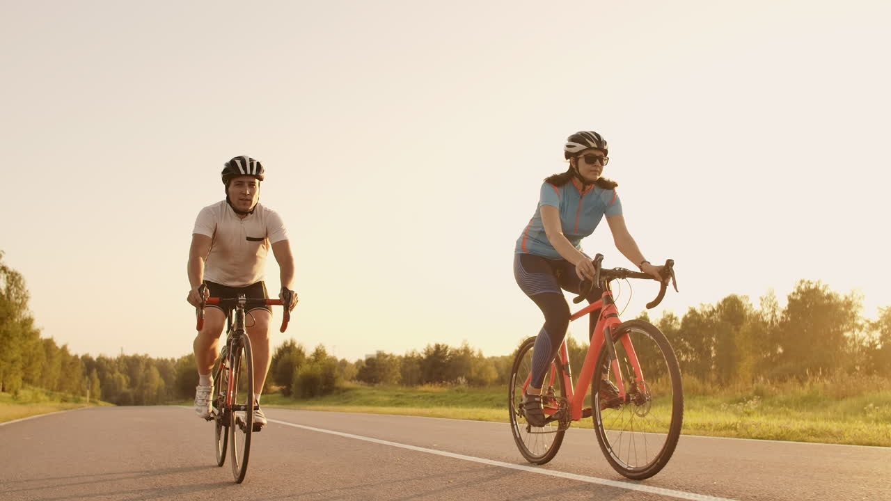 A man and a woman ride sports bikes on the highway at sunset in gear and protective helmets in slow motion 120 fps.