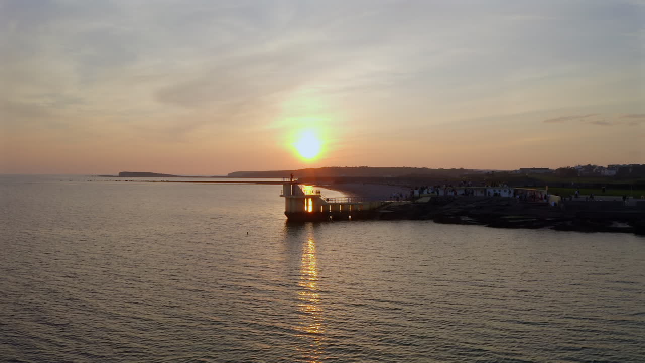 Slow motion tracking left of diving tower as sun nears horizon and waves gently break