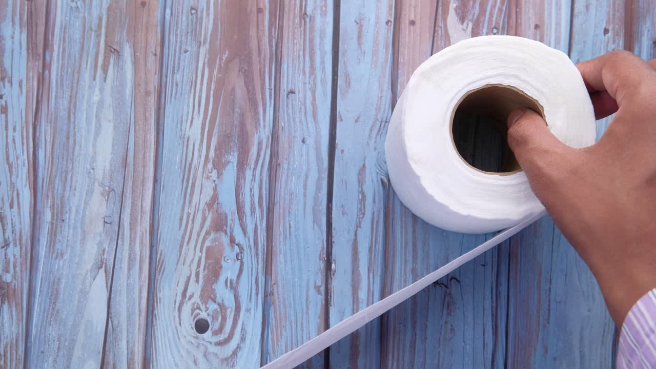 mano tirando papel higiénico de un rollo en una mesa de madera