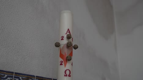 primer plano de una vela pascual adornada con elementos simbólicos contra una pared texturizada
