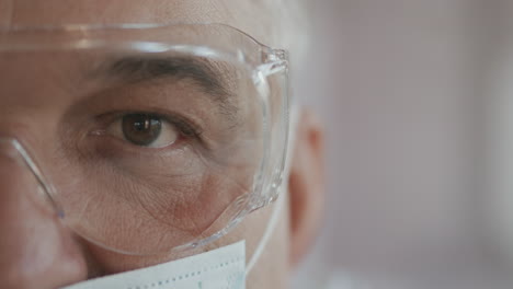 male doctor or nurse in uniform mask and glasses looking straight at camera. close up of eye. slow motion