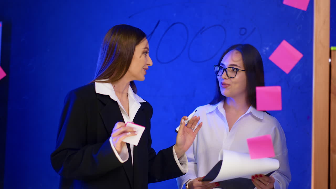 Caucasian women discussing numbers at the glass wall. Colleagues share ideas, building strategies and plan.