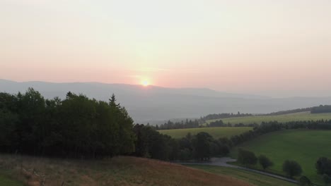 Drone-shot-of-sunrise-above-hills,-forest-and-mountains-in-Czech-countryside