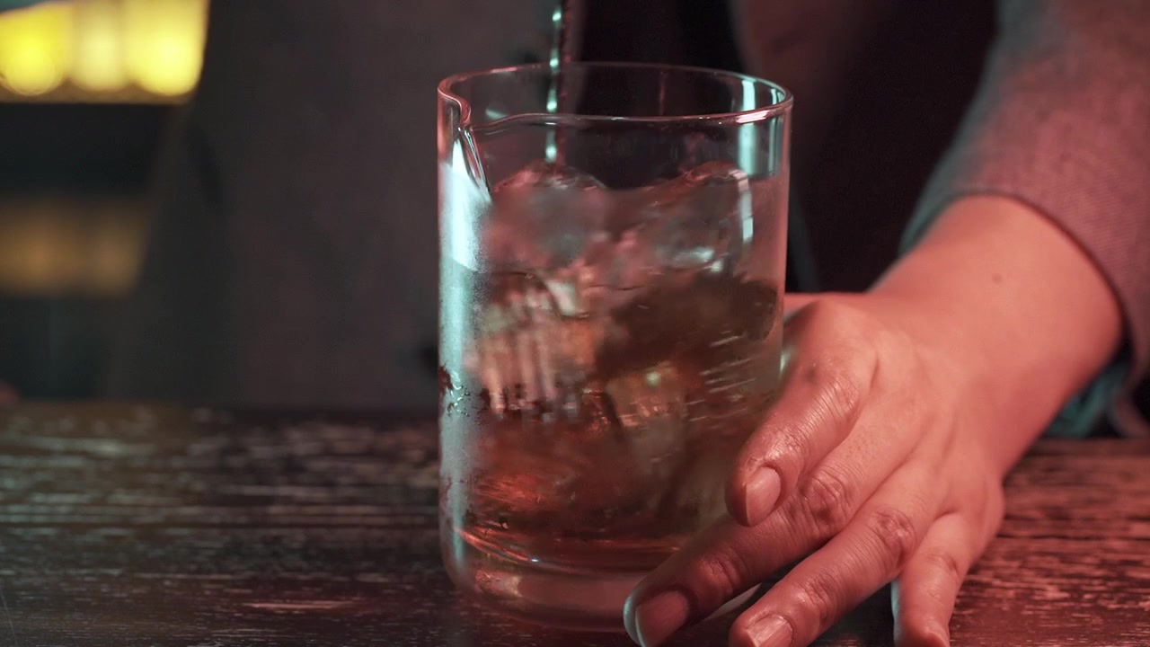 Primo piano di un barista che mescola un cocktail elegante al rallentatore al bar.