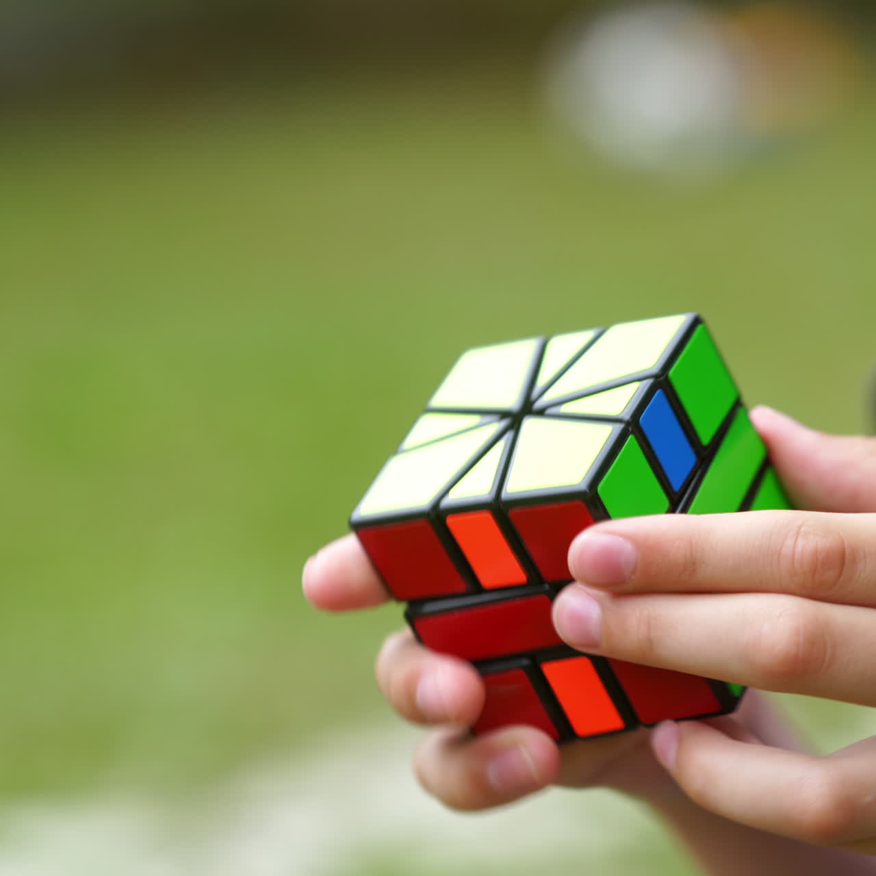 Close-up of rubik's cube in boy's hands. Boy is holding rubik cube and solving puzzle of one of the world's best-selling toys on blur green background.