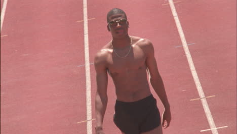 a man walks off a racing field with shoes in hand