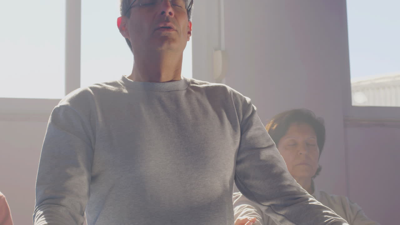 체육관에서 눈을 감고 롯스 자세로 앉아 있는 노인 들