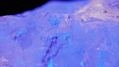 crystal clear quartz illuminated by cool ice purple light on dark background, captured through smooth panning and macro lens