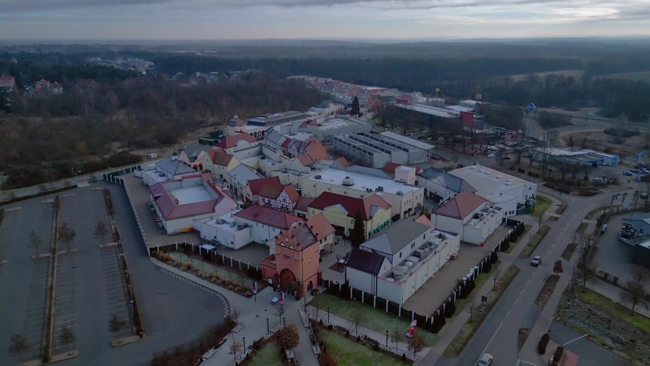 Un grande centro commerciale outlet con più edifici, negozi al dettaglio e un parcheggio vuoto. Spettacolare vista aerea panoramica in ascesa con drone.