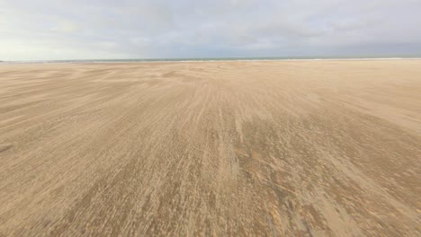 Drone-Volando-Hacia-El-Mar-En-Una-Playa-De-Arena-Vacía,-Volando-Por-Un-Parque-Infantil-En-Vrouwenpolder,-Países-Bajos