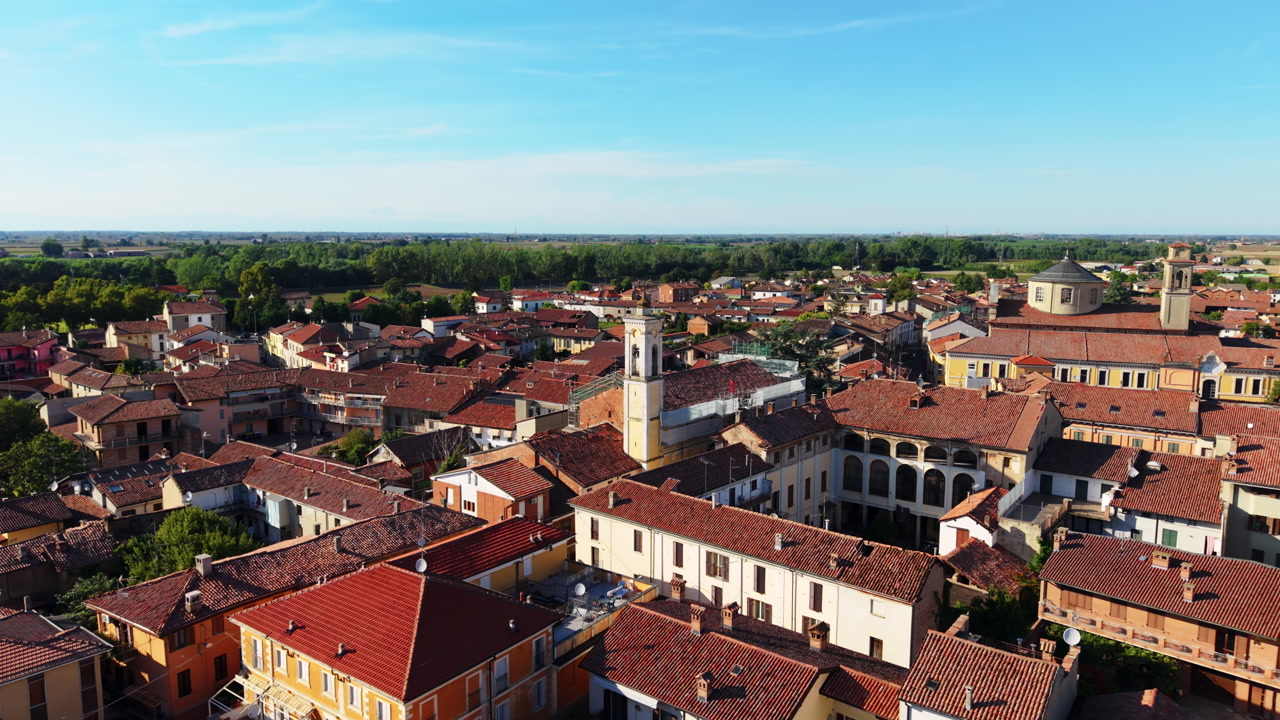 Drone advances over medieval town, passing stone tower toward church in Piedmont.