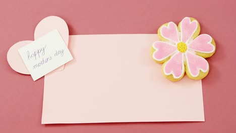 flower shape cookie, heart shape card on red envelope against pink background