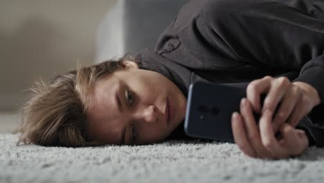 caucasian sad woman using mobile phone and lying down on carpet.