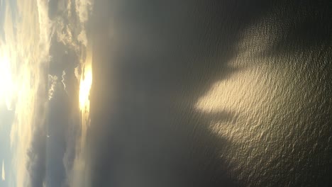 Vertical video of a serene sunset from a plane window, with magical light reflections on the ocean