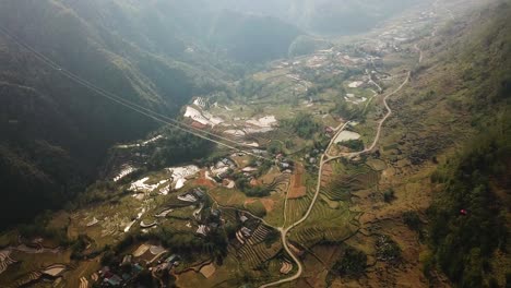 a wide aerial shot panning above two cable cars as they journey high above a huge farming valley in sapa vietnam